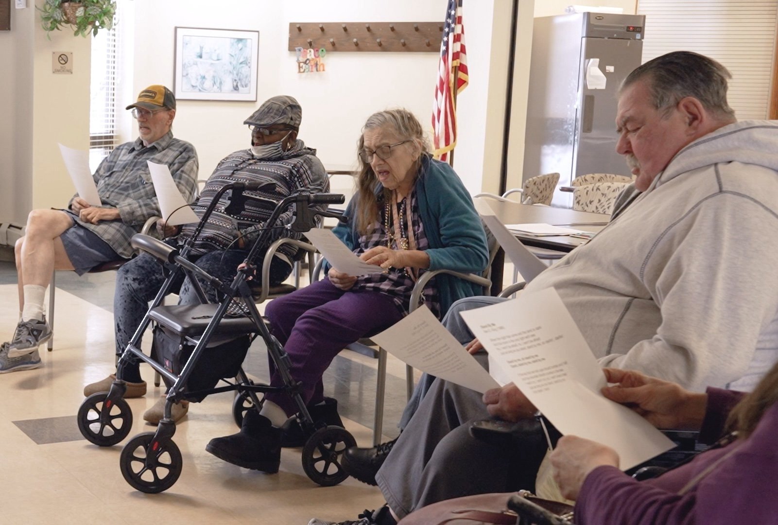 A small group of seniors gathered in a circle, some using mobility aids, engaged in a music session